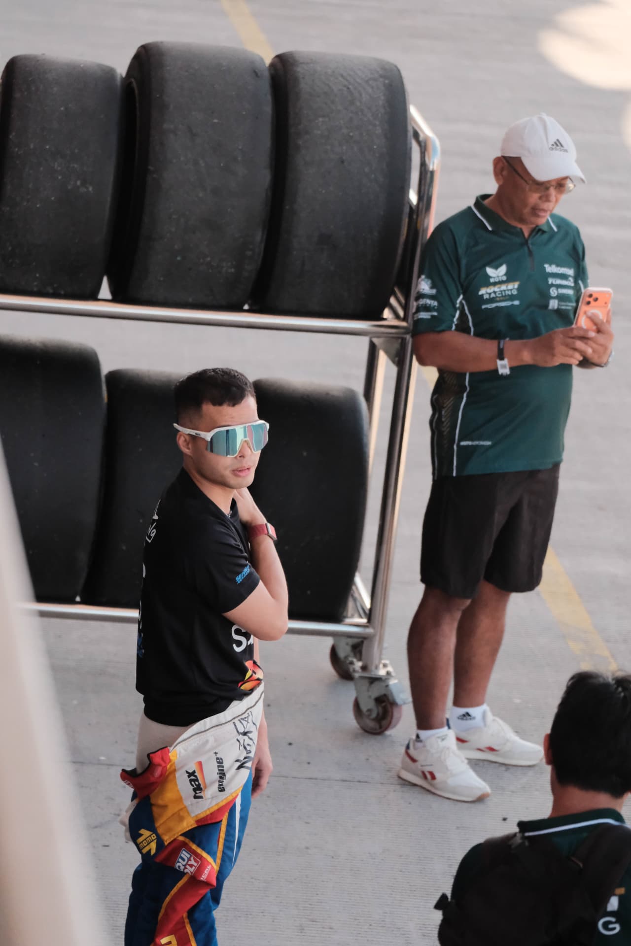 Driver and team member waiting beside a rack of slick tyres