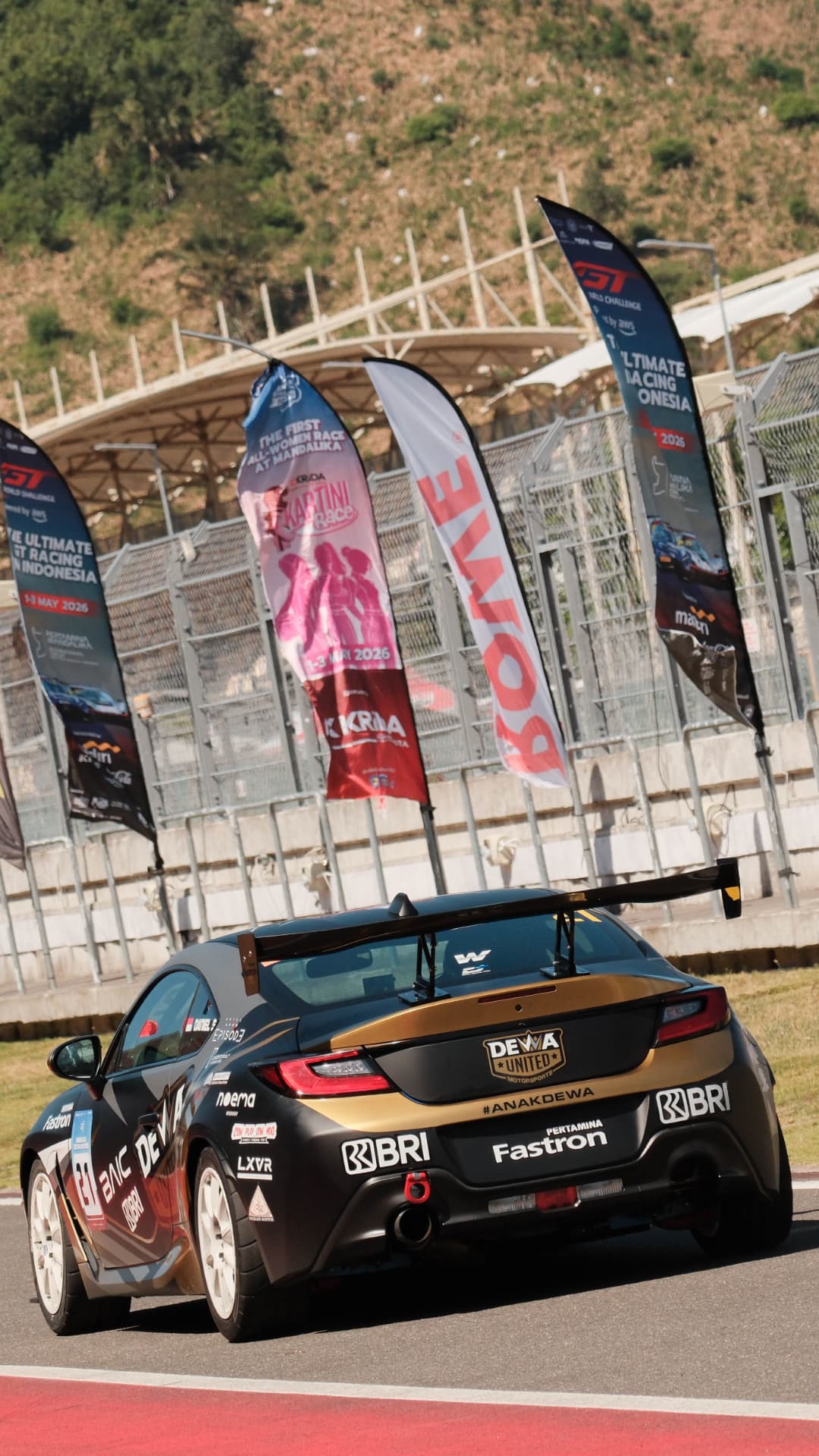 Black and gold Dewa United GT car on track beneath event flags