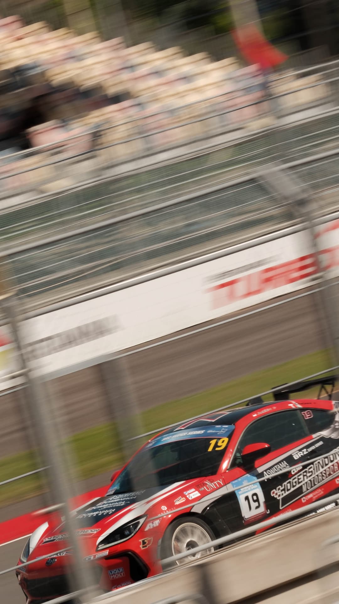 Red number 19 BRZ seen through the catch fencing at speed